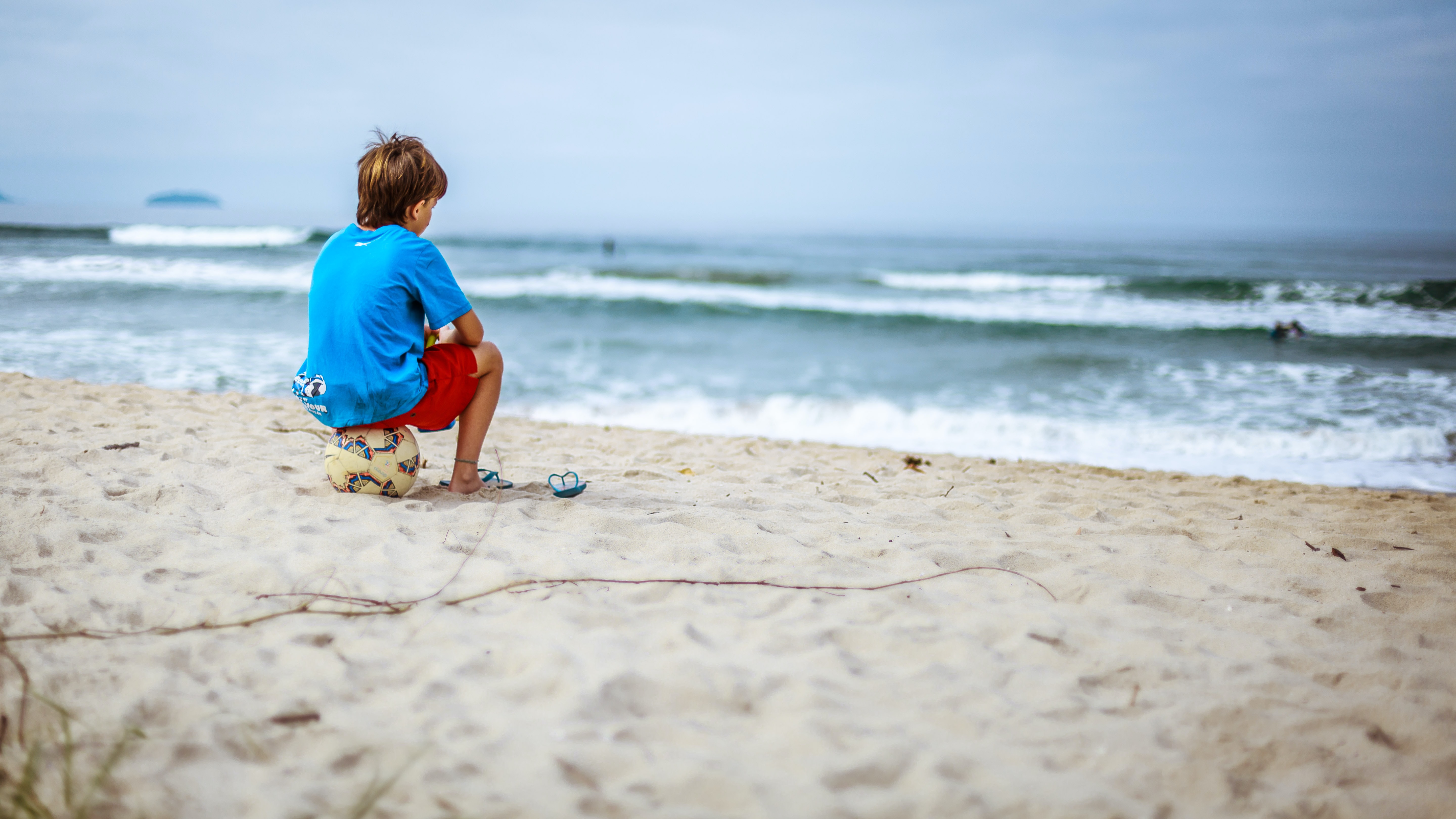 Ensamt barn sitter på en fotboll på stranden