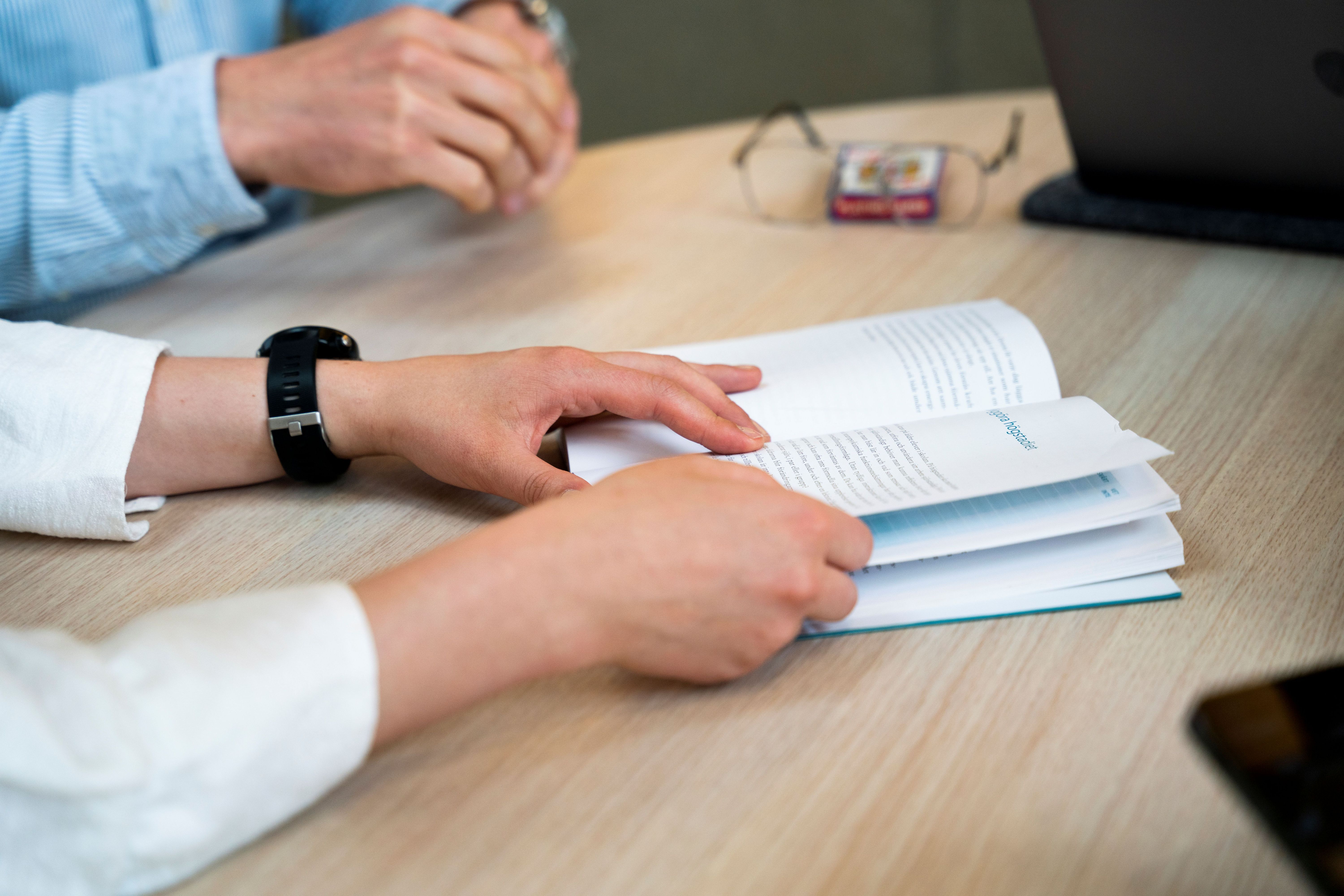 Två par händer på ett bord med en bok emellan 