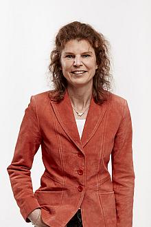 Portrait of a smiling woman wearing an orange blazer, standing against a plain white background.